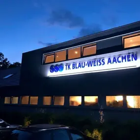 Beleuchtetes Vereinsgebäude mit Schriftzug TK Blau-Weiss Aachen bei Dämmerung
