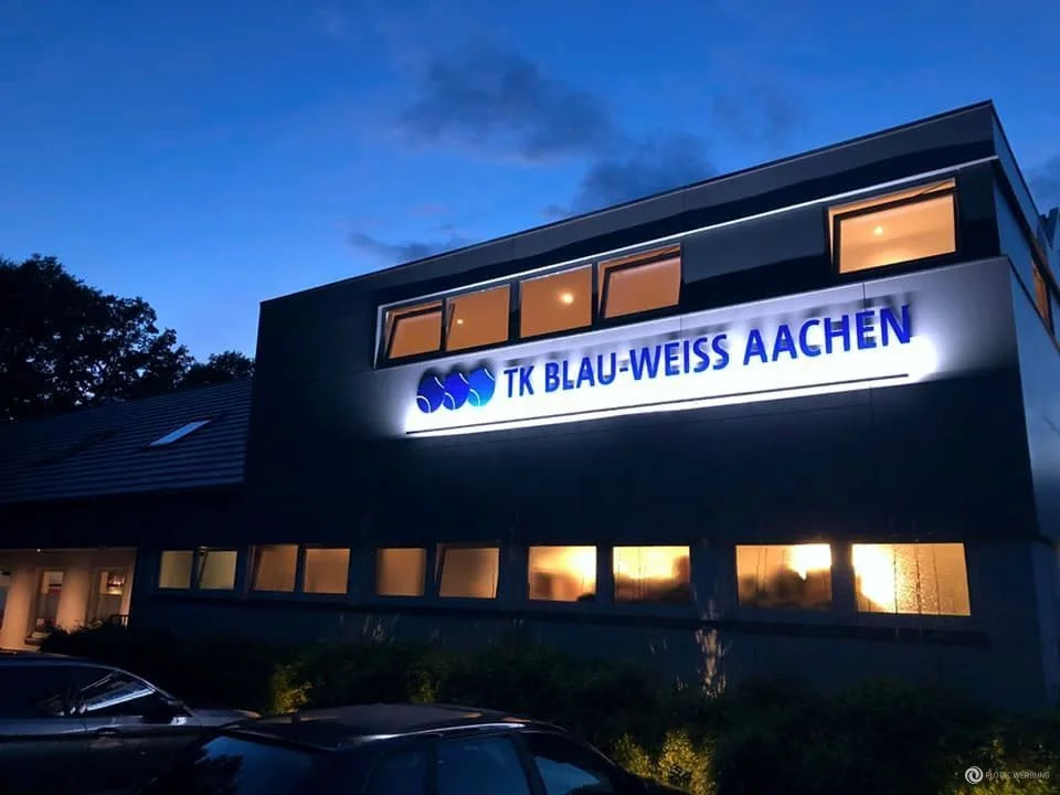 Beleuchtetes Vereinsgebäude mit Schriftzug TK Blau-Weiss Aachen bei Dämmerung