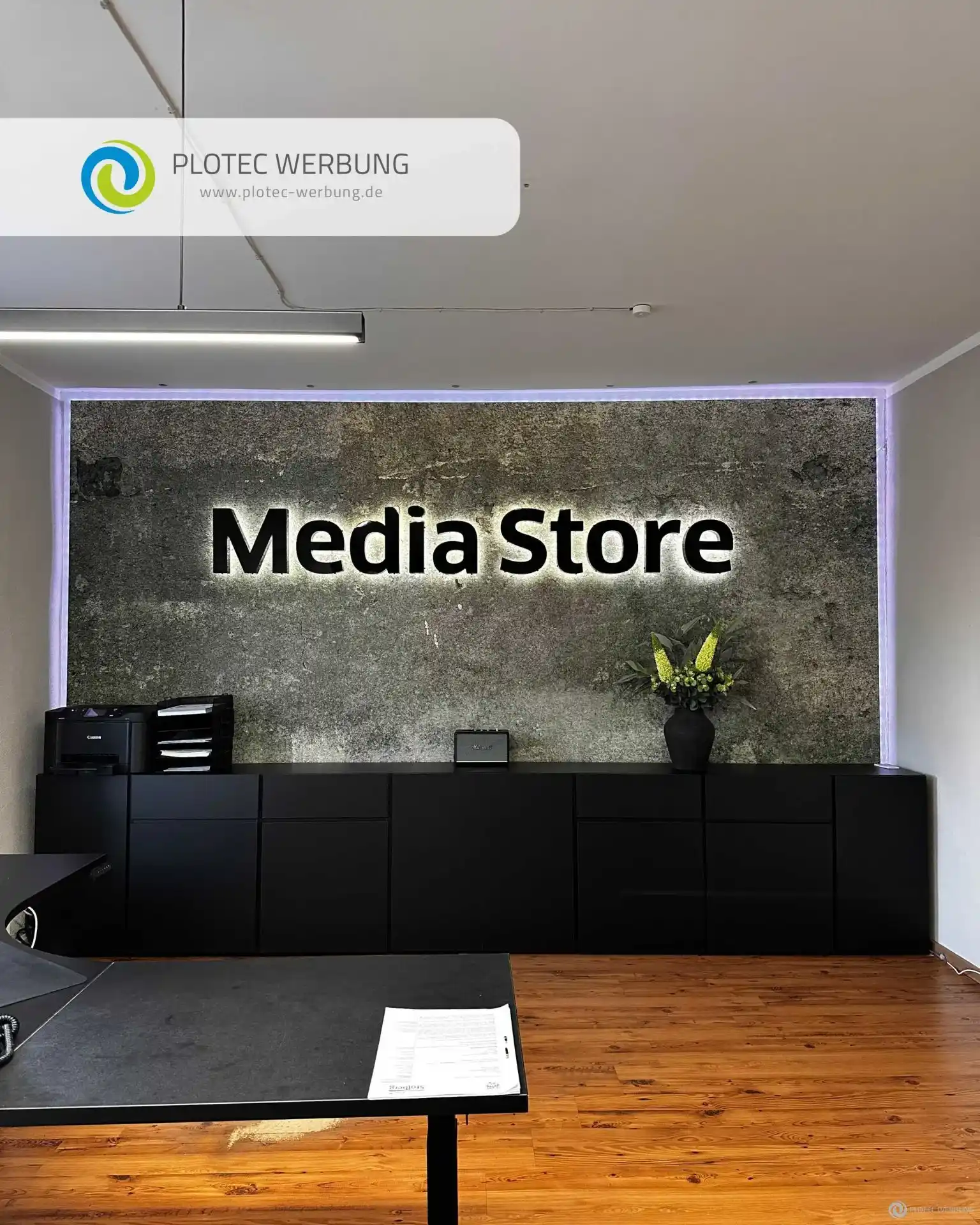 Beleuchteter Media Store Schriftzug an Betonwand im modernen Empfangsbereich